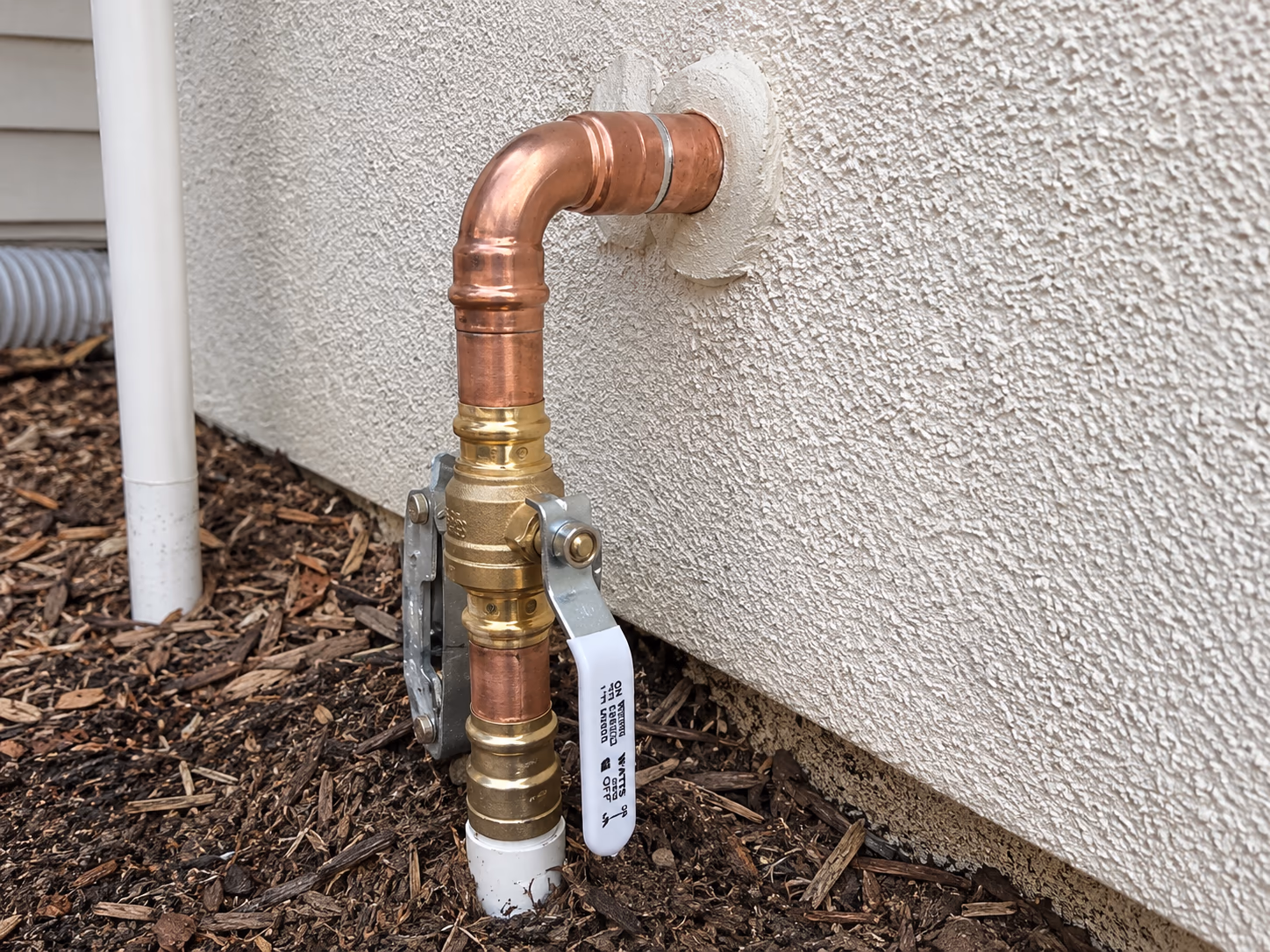 New residential main water shut-off valve replacement with copper line and brass quarter-turn ball valve installed on a Sacramento home exterior