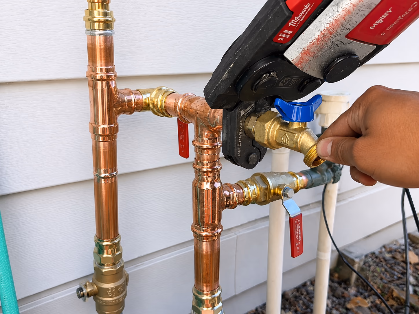 Plumber installing a new outdoor hose bib spigot with copper press fittings and a brass shut-off valve on a residential exterior wall