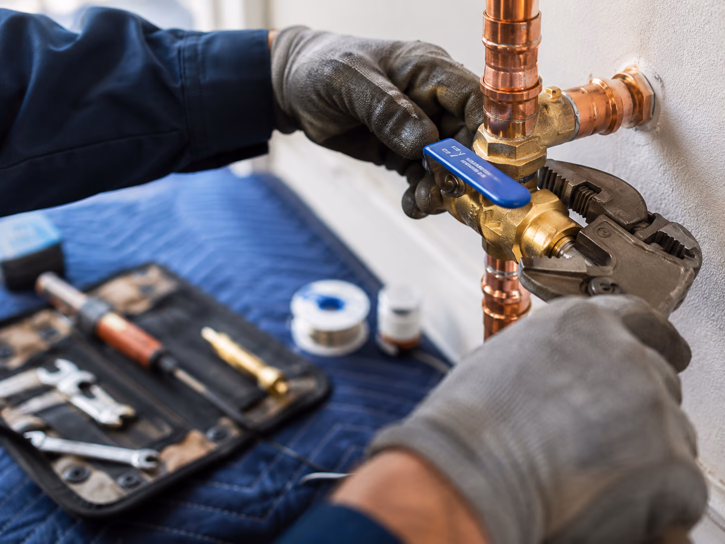 Plumber installing a new brass quarter-turn ball valve with a blue lever onto a residential copper main water line